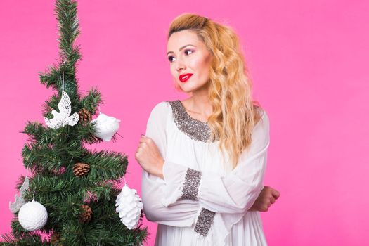 Christmas and people concept - young blonde woman thinking about next year near the christmas tree over the pink background.