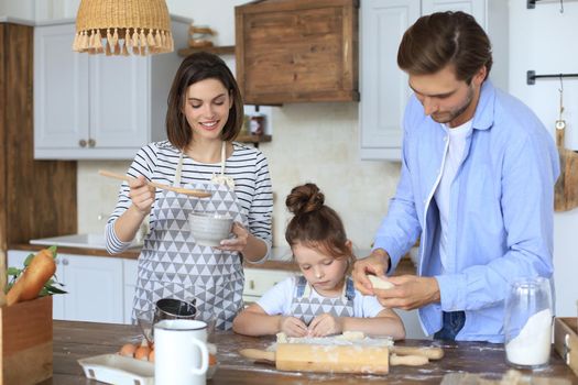 Cute little girl and her parents are having fun while cooking in kitchen at home together