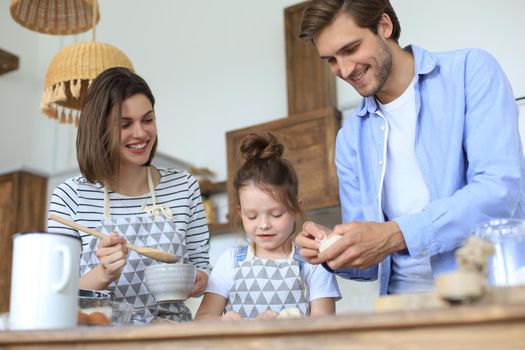 Cute little girl and her parents are having fun while cooking in kitchen at home together