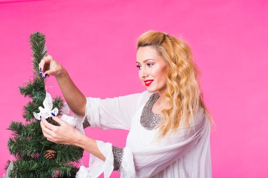 People, holidays and christmas concept - woman decorating christmas tree on pink background.