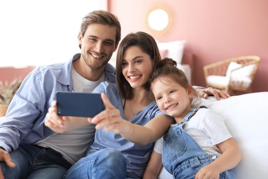 Beautiful young family with little child taking a selfie with a smartphone at home on the couch