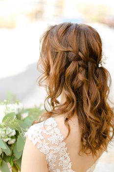 Back view of brown curls for bride keeping flowers. Concept of wedding photo session and stylish hair do.