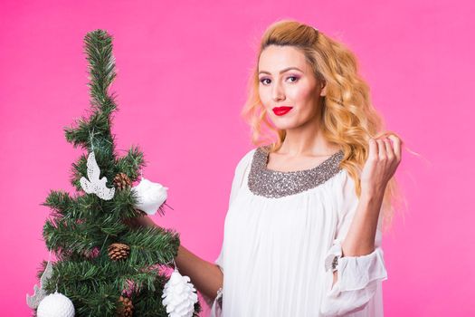 Young happy woman near christmas tree on pink background.