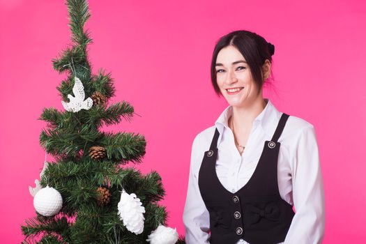 Young happy woman near christmas tree on pink background.