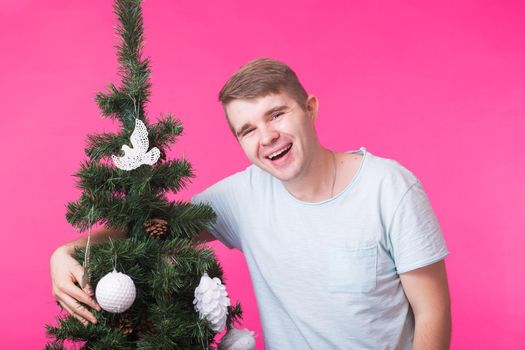 Holidays and people concept - Happy man with christmas tree on pink background.