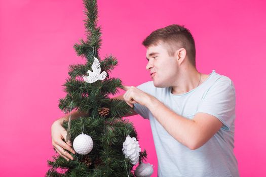 People, holidays and christmas concept - young man decorating christmas tree on pink background.