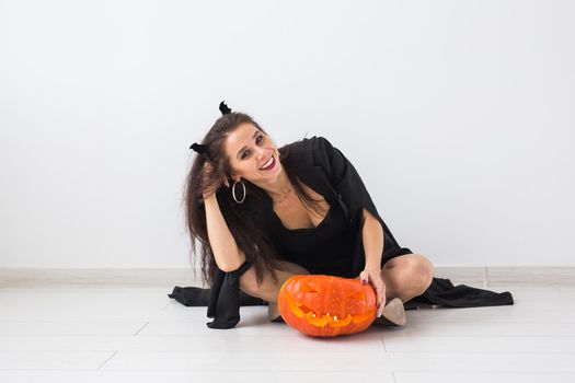 Happy gothic young woman in witch halloween costume smiling over white room background.