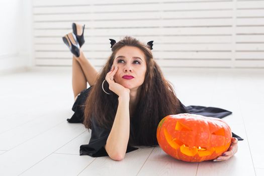 Happy gothic young woman in witch halloween costume smiling over white room background.