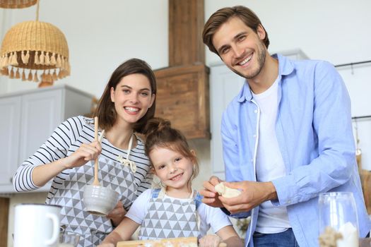 Cute little girl and her parents are having fun while cooking in kitchen at home together