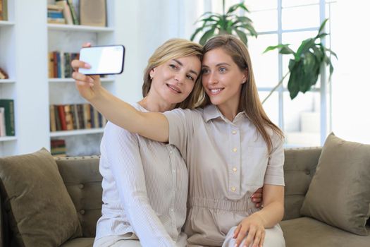 Happy middle aged mother and daughter taking selfie at home