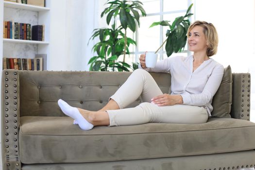 Mature blond woman in couch having a tea or coffee