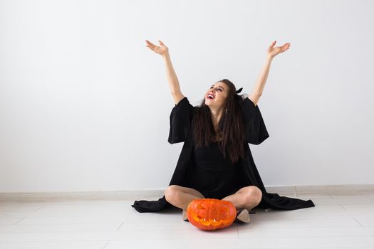 Excited happy young woman in halloween costume posing with carved pumpkin in lightroom.