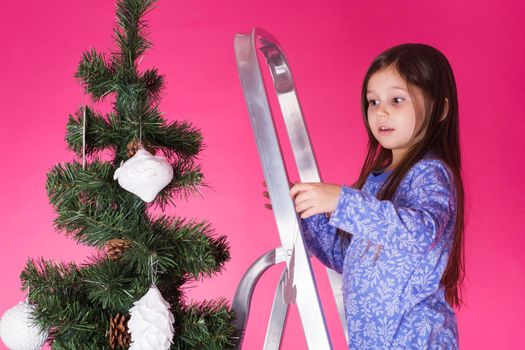 Little girl with christmas tree on pink background.