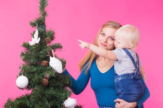 Christmas, holidays and people concept - young happy woman with her daughter on hands show decorations on christmas tree.