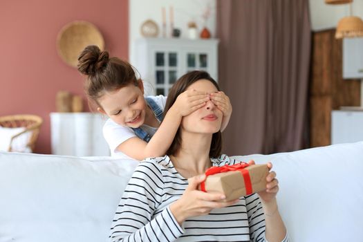 Little girl make birthday present to excited parent , smiling little child congratulate give gift box to happy mother and closed mother's eyes