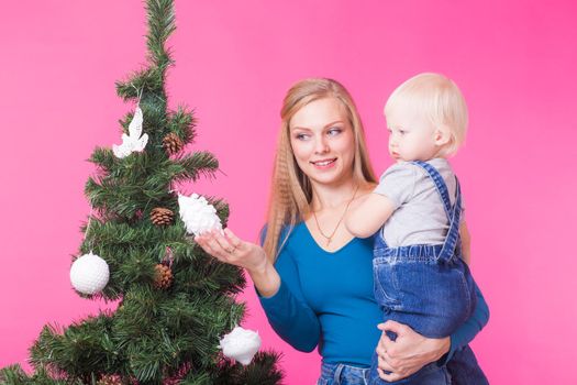 Christmas, holidays and people concept - young happy woman with her daughter on hands show decorations on christmas tree.
