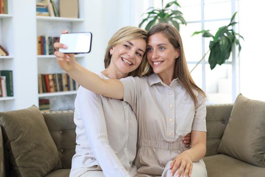 Happy middle aged mother and daughter taking selfie at home