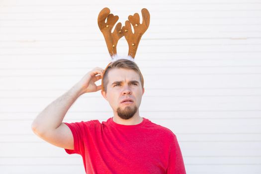 Christmas, holidays and people concept - a man's head with deer horns on it. Man scratches his head.