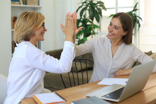 Middle aged businesswoman giving high five to her young female collegue