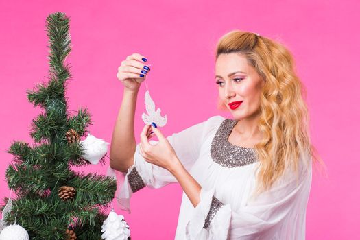 People, holidays and christmas concept - woman decorating christmas tree on pink background.