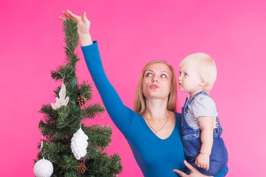 Christmas, holidays and people concept - young happy woman with her daughter on hands show decorations on christmas tree.