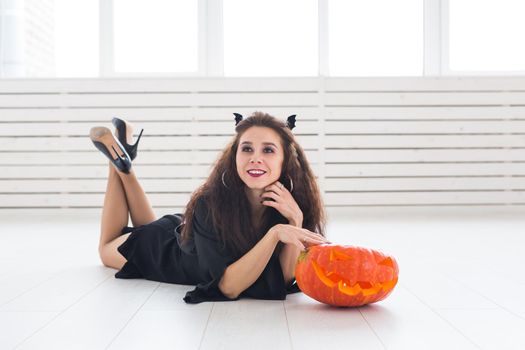 Happy gothic young woman in witch halloween costume smiling over white room background.