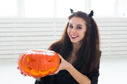 Smiling brunette woman in halloween makeup posing with carved pumpkin.