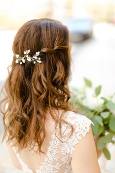 Back view of nice brown curls for bride keeping flowers. Concept of wedding photo session and stylish hair do.