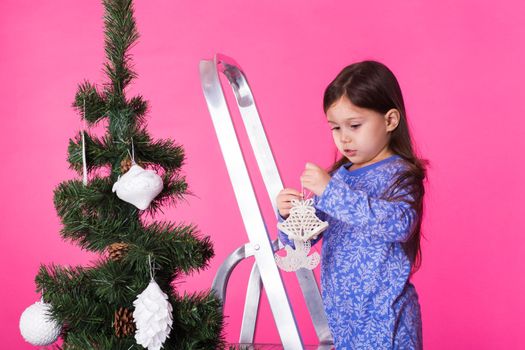 Little girl with christmas tree on pink background.