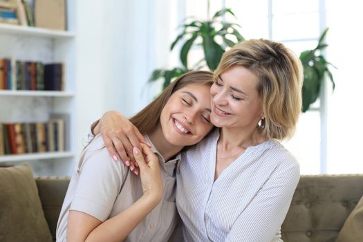 Cheerful young woman is embracing her middle aged mother in living room
