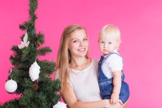 Christmas and holiday concept - Portrait of smiling woman with her little daughter decorating Christmas tree over pink background.