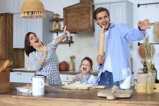 Cute little girl and her parents are having fun while cooking in kitchen at home together