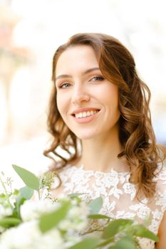 Portrait of beautiful smiling fiancee keeping flowers. Concept of bridal makeup, wedding photo session.
