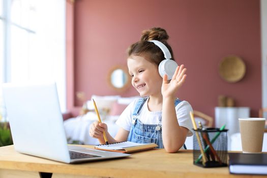 Distance learning. Cheerful little girl girl in headphones using laptop studying through online e-learning system.