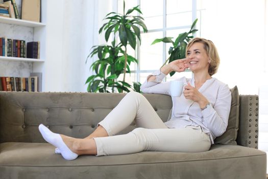 Mature blond woman in couch having a tea or coffee