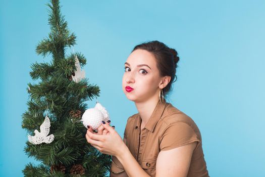 Christmas, holidays and people concept - young happy woman decorating christmas tree on blue background.