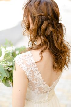 Back view of curls for bride keeping flowers. Concept of wedding photo session and stylish hair do.