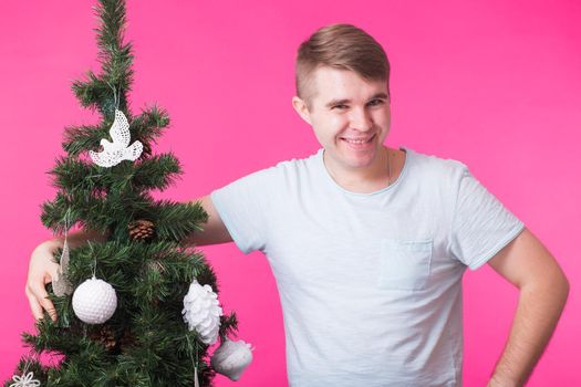 Christmas and holiday concept - Laughing man hugs Christmas tree over pink background.
