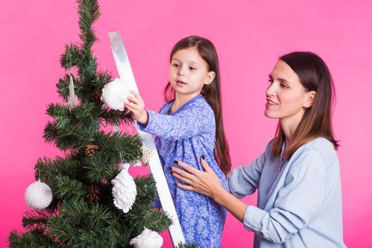 Christmas of young mom and her daughter with Christmas tree on pink background.