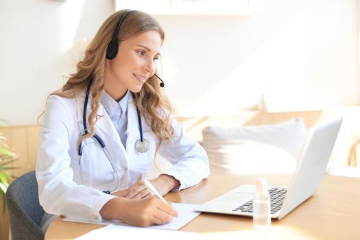 Friendly doctor working online with a laptop sitting in a desk in a consultation