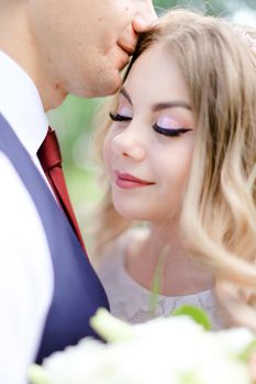 Portrait of happy groom with red tie kissing bride. Concept of married couple and love.