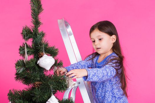 Little girl with christmas tree on pink background.