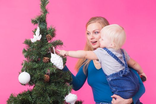 Christmas and holiday concept - Portrait of smiling woman with her little daughter decorating Christmas tree over pink background.