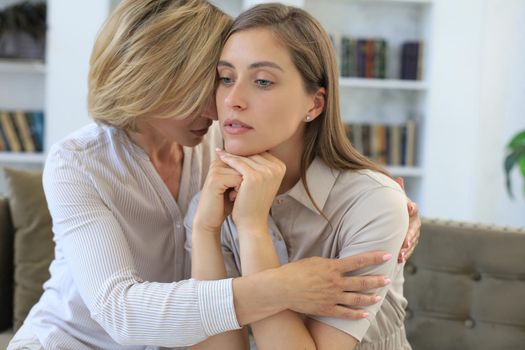 Concerned middle aged mother and adult daughter sit on couch having serious conversation, listen to her sharing problems.