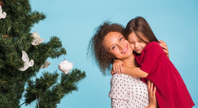 Christmas of young mom and her daughter with Christmas tree on blue background.