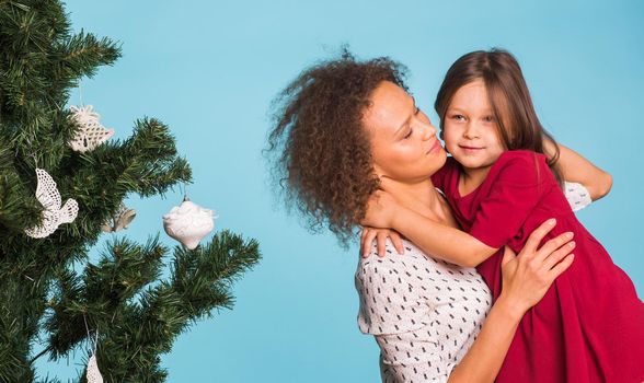 Christmas of young mom and her daughter with Christmas tree on blue background.