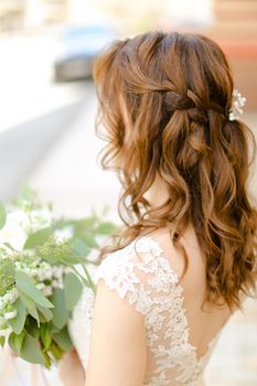 Back view of nice curls for bride keeping flowers. Concept of wedding photo session and stylish hair do.