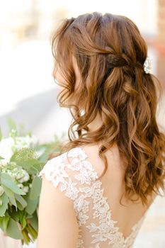 Back view of cute curls for bride keeping flowers. Concept of wedding photo session and stylish hair do.