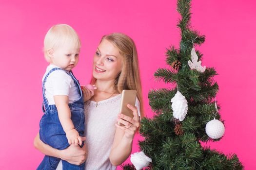 Mother and little daughter taking a selfie near Christmas tree.