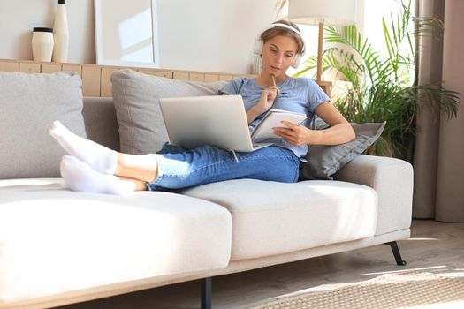 Smiling young woman with headphones and laptop on the sofa